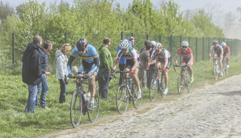 Carrefour de l'Arbre,France-April 13,2014: The junior cyclist Enzo Wouters in front of a part of the peloton,containing young cyclists, riding during a race of juniors on the cobblestoned road in the dust, few hours before the famous official one day race Paris - Roubaix. Wouters finished the race in the third position. Carrefour de l'Arbre,France-April 13,2014: The junior cyclist Enzo Wouters in front of a part of the peloton,containing young cyclists, riding during a race of juniors on the cobblestoned road in the dust, few hours before the famous official one day race Paris - Roubaix. Wouters finished the race in the third position.