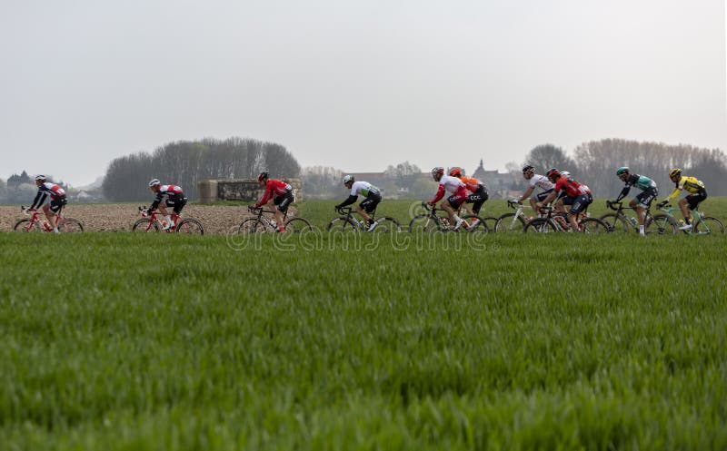 Viesly, France - April 14, 2019: The peloton riding on the dusty cobblestone road from Cysoing to Bourghelles during Paris Roubaix 2019. Viesly, France - April 14, 2019: The peloton riding on the dusty cobblestone road from Cysoing to Bourghelles during Paris Roubaix 2019