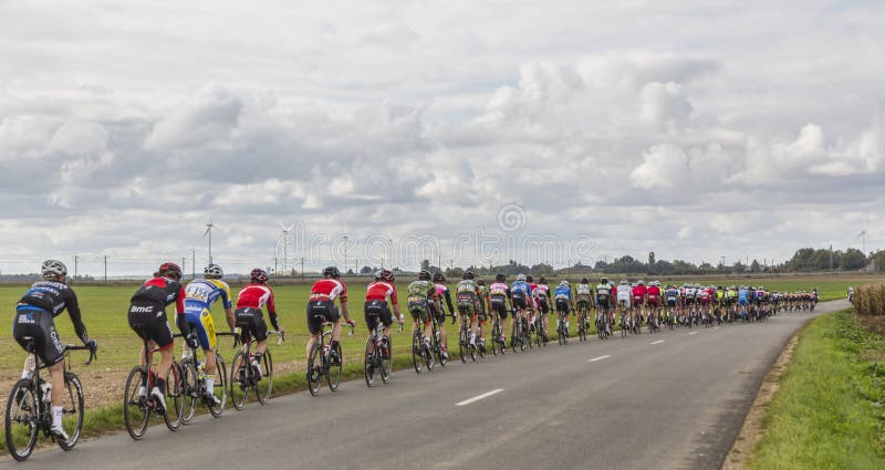 Le Gault-Saint-Denis, France - October 08, 2017: The peloton riding on a road in the plain with windmills in a cloudy day during the Paris-Tours road-cycling race. Le Gault-Saint-Denis, France - October 08, 2017: The peloton riding on a road in the plain with windmills in a cloudy day during the Paris-Tours road-cycling race.