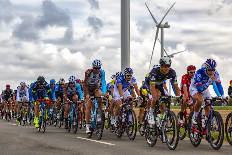 Le Gault-Saint-Denis, France - October 08, 2017: The peloton riding on a road in the plain with windmills in a cloudy day during the Paris-Tours road-cycling race. Le Gault-Saint-Denis, France - October 08, 2017: The peloton riding on a road in the plain with windmills in a cloudy day during the Paris-Tours road-cycling race