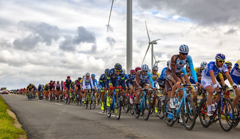 Le Gault-Saint-Denis, France - October 08, 2017: The peloton riding on a road in the plain with windmills in a cloudy day during the Paris-Tours road-cycling race. Le Gault-Saint-Denis, France - October 08, 2017: The peloton riding on a road in the plain with windmills in a cloudy day during the Paris-Tours road-cycling race