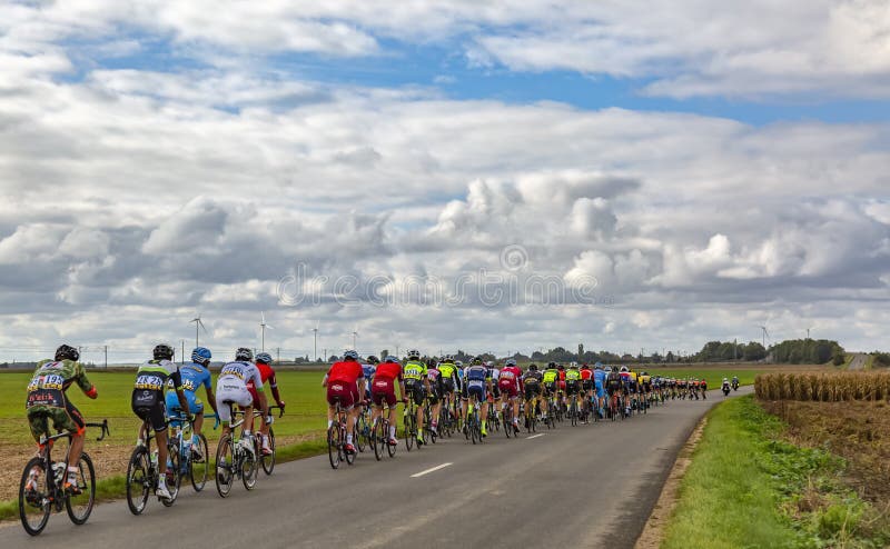 Le Gault-Saint-Denis, France - October 08, 2017: The peloton riding on a road in the plain with windmills in a cloudy day during the Paris-Tours road-cycling race. Le Gault-Saint-Denis, France - October 08, 2017: The peloton riding on a road in the plain with windmills in a cloudy day during the Paris-Tours road-cycling race