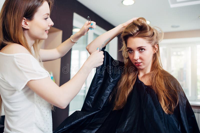 Peluquero de sexo femenino sonriente que hace tocado a la mujer bastante joven con el pelo justo largo en salón de la peluquería imagen de archivo libre de regalías Peluquero de sexo femenino sonriente que hace tocado a la mujer bastante joven con el pelo justo largo en salón de la peluquería imagen de archivo libre de regalías