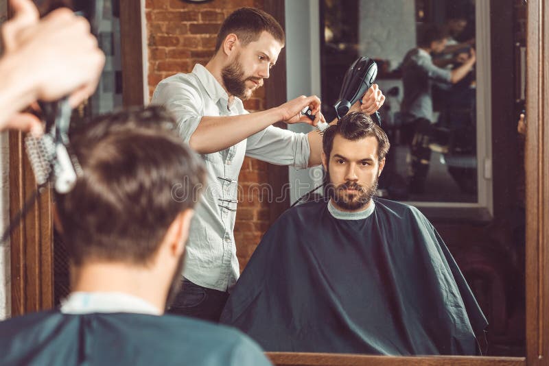 Peluquero hermoso joven que hace corte de pelo de hombre atractivo en barbería imagenes de archivo Peluquero hermoso joven que hace corte de pelo de hombre atractivo en barbería imagenes de archivo