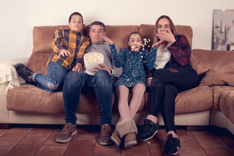 Película de terror de observación de la familia en el sofá en casa y comiendo las palomitas imagen de archivo libre de regalías Película de terror de observación de la familia en el sofá en casa y comiendo las palomitas imagen de archivo libre de regalías