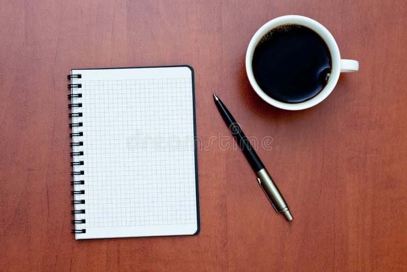 Pen on a white spiral notebook with cup of coffee