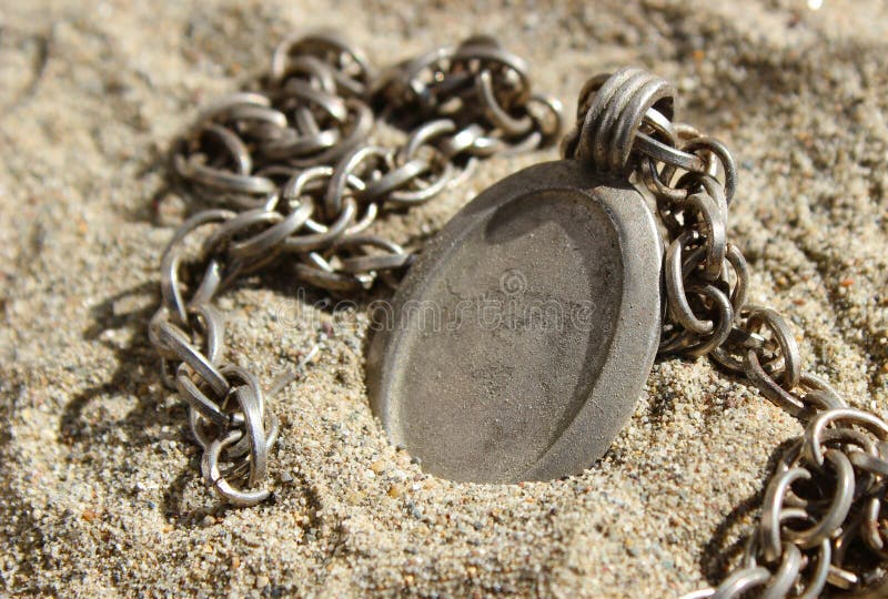 A rustic steel metal photo locket with chain, lying in sand. The pendant is blank and the space can be used to insert text or image. Suitable for concepts like - finding treasure,. A rustic steel metal photo locket with chain, lying in sand. The pendant is blank and the space can be used to insert text or image. Suitable for concepts like - finding treasure,