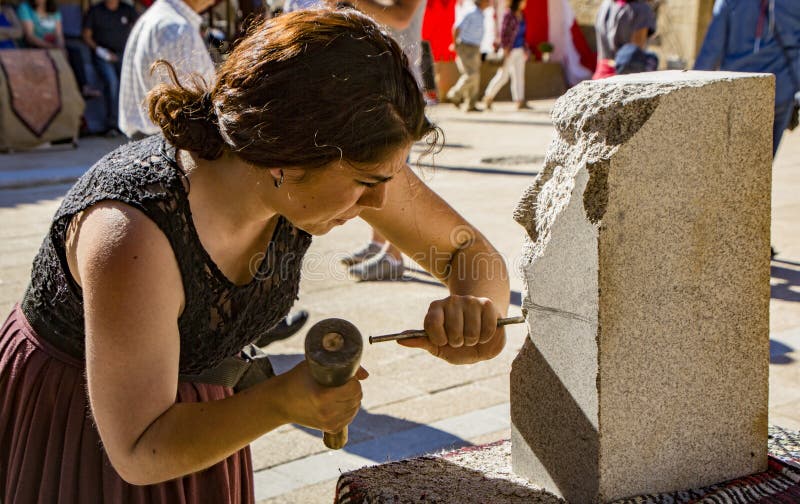 Penedono , Portugal - July 1, 2017 - Woman carves new sculpture in annual Medieval fair from a block of granite. Penedono , Portugal - July 1, 2017 - Woman carves new sculpture in annual Medieval fair from a block of granite