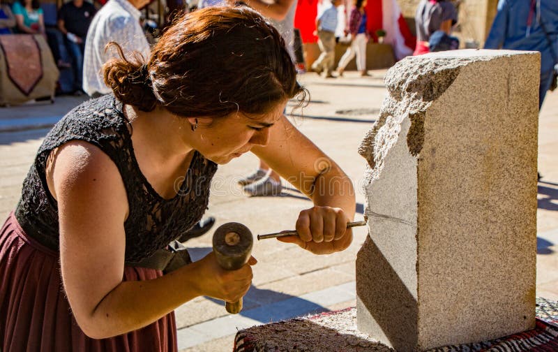 Penedono , Portugal / July 1, 2017 - Woman carves new sculpture in annual Medieval fair from a block of granite. Penedono , Portugal / July 1, 2017 - Woman carves new sculpture in annual Medieval fair from a block of granite