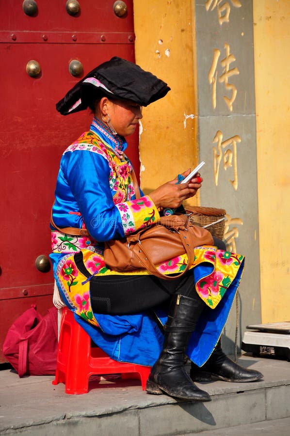 Chinese woman wearing the traditional clothing of the Qiang people sitting in front of the Long Xing Monastery's front door in Pengzhou, China. Chinese woman wearing the traditional clothing of the Qiang people sitting in front of the Long Xing Monastery's front door in Pengzhou, China.