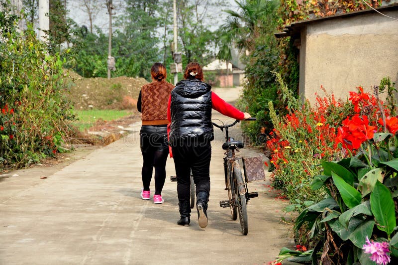 Pengzhou, Китай: 2 велосипеда женщин идя на проселочной дороге