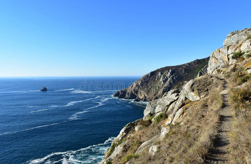 Penhasco com trajeto Rochas e mar azul com espuma, dia ensolarado Finisterre, Galiza, Espanha imagens de stock Penhasco com trajeto Rochas e mar azul com espuma, dia ensolarado Finisterre, Galiza, Espanha imagens de stock