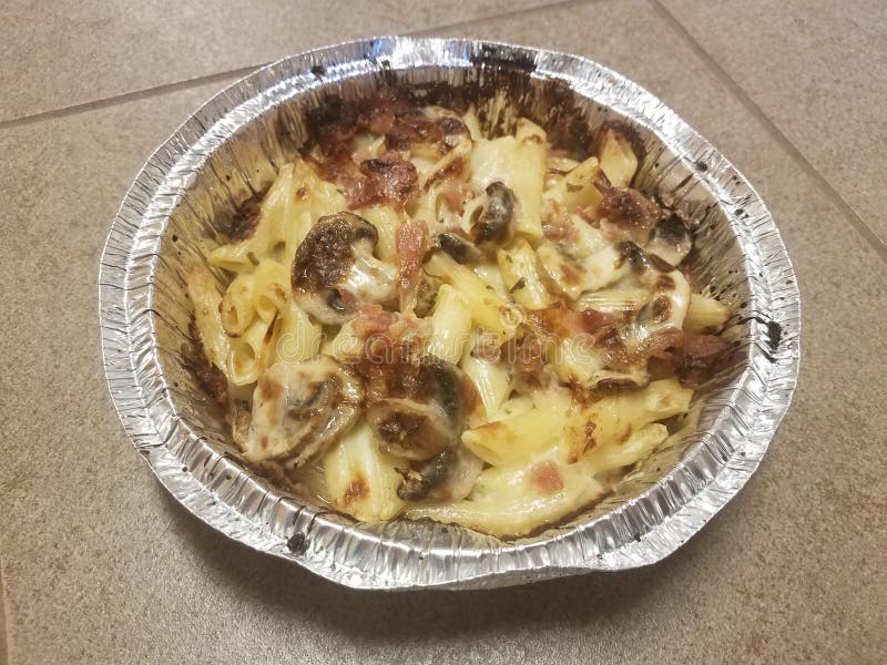 Penne Pasta with Bacon and Mushrooms in Foil Plate on Tile Floor Stock