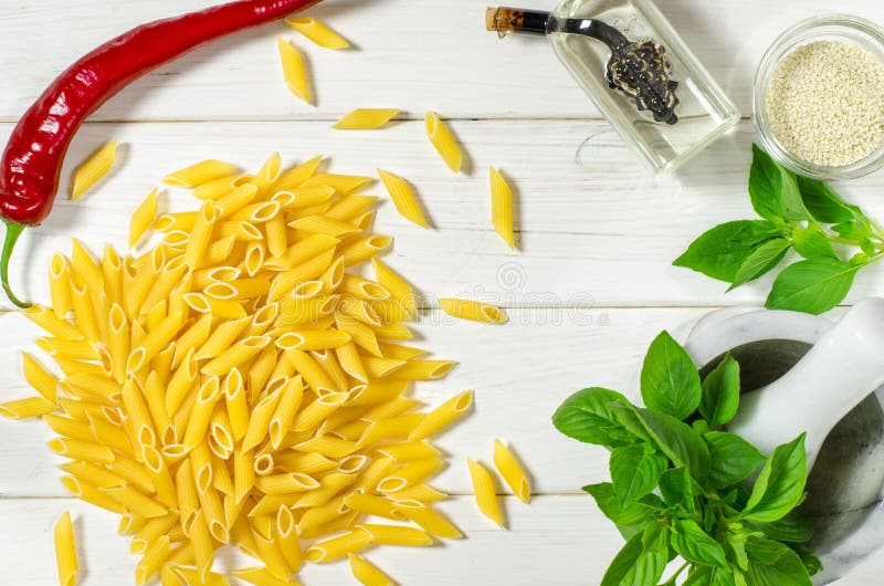 Penne Pasta, grüne Basilika, Parmesan, Sesam, Knoblauch, Chili, Eier liegen auf einem weißen Tisch stockbild
