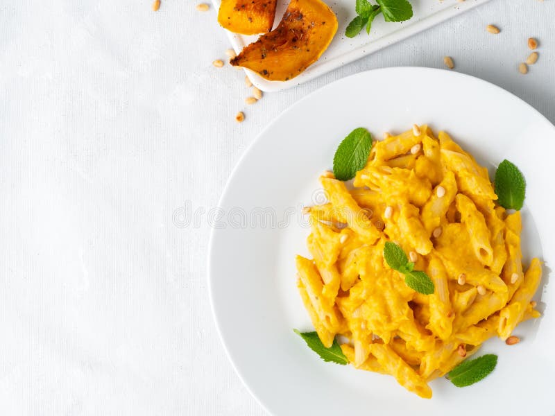 Penne макаронных изделий тыквы со сметанообразным соусом испеченного сквоша на белой предпосылке, взгляде сверху, космосе экземпл стоковые изображения rf Penne макаронных изделий тыквы со сметанообразным соусом испеченного сквоша на белой предпосылке, взгляде сверху, космосе экземпл стоковые изображения rf