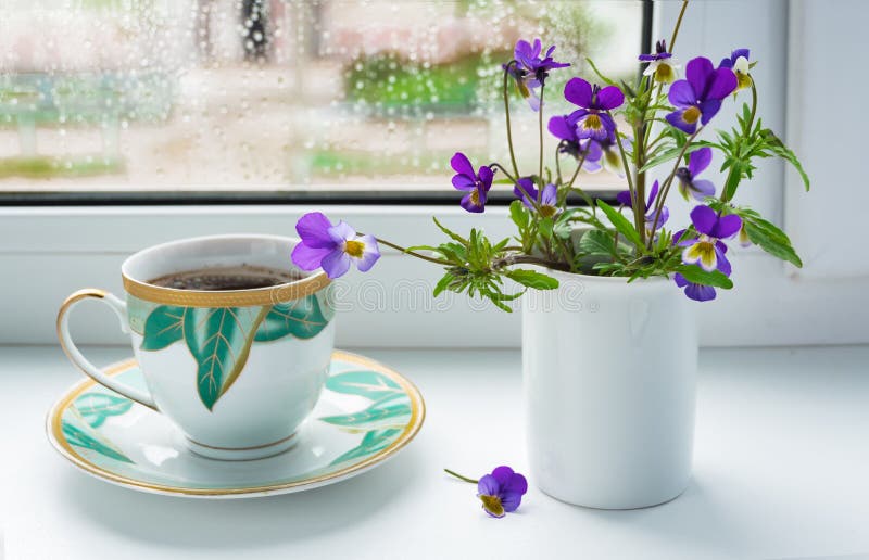Pensamientos de las flores salvajes y una taza de café en el alféizar en tiempo lluvioso imagen de archivo libre de regalías Pensamientos de las flores salvajes y una taza de café en el alféizar en tiempo lluvioso imagen de archivo libre de regalías