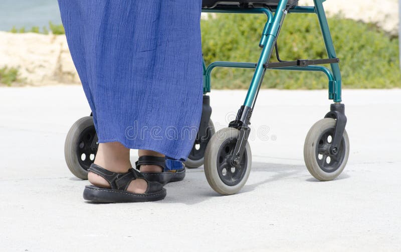 A disabled old woman is strolling along a footpath with a walking aid. A disabled old woman is strolling along a footpath with a walking aid.