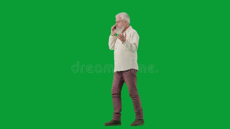 Portrait of aged bearded man on chroma key green screen. Full shot senior man walking and talks on smartphone. Half turn