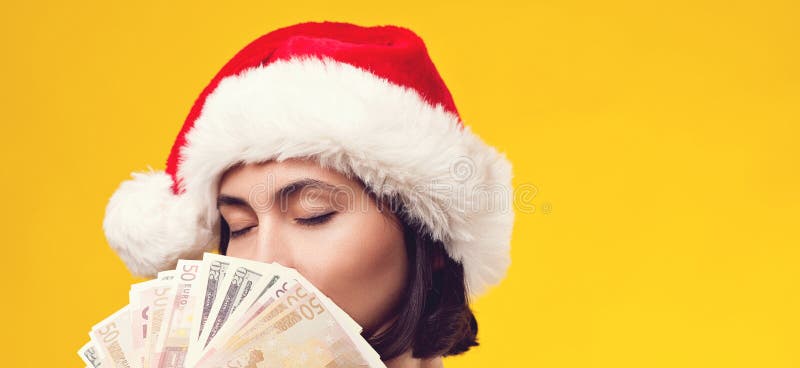 Pensive brunette woman in christmas hat holding money. Girl dreaming in Christmas. Isolated on yellow background, copy space. royalty free stock images Pensive brunette woman in christmas hat holding money. Girl dreaming in Christmas. Isolated on yellow background, copy space. royalty free stock images