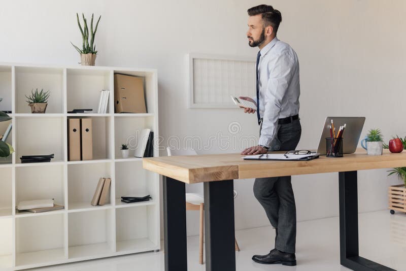 Pensive Businessman With Calculator In Hand Standing At Table