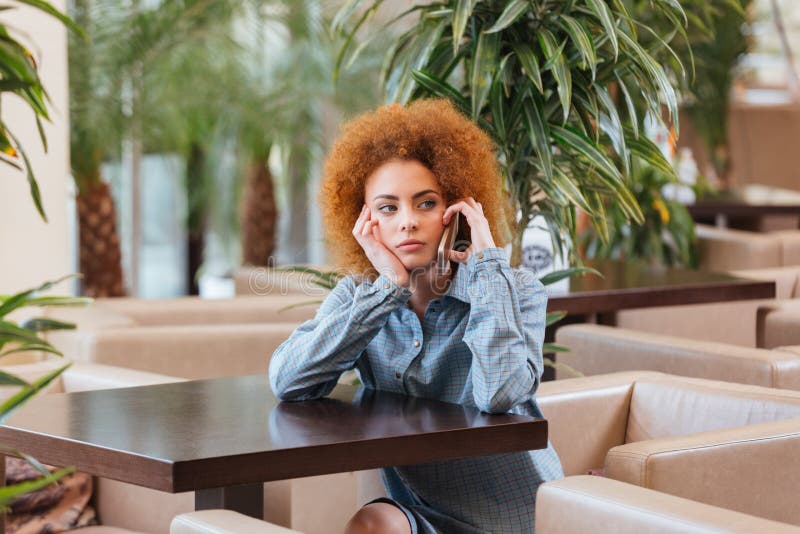 Pensive curly woman talking on cell phone in cafe stock photos