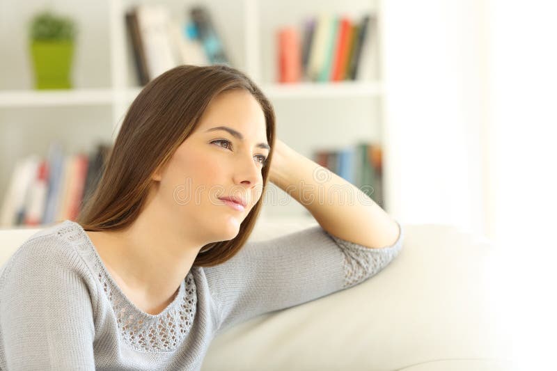 Pensive Frau sitzt zu Hause auf einem Sofa
