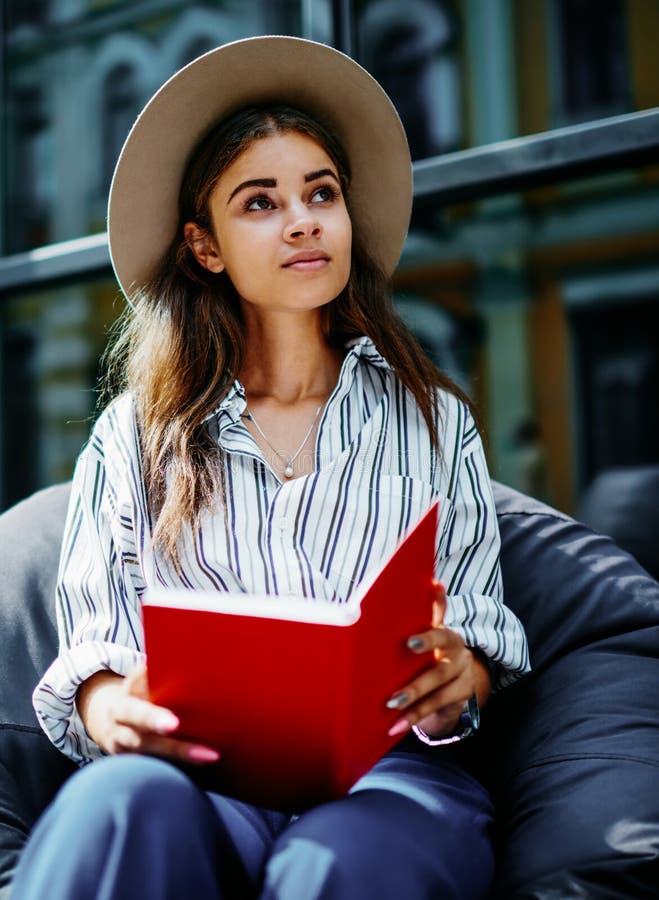 Pensive hipster fille assise à l'extérieur avec livre levant photographie stock libre de droits