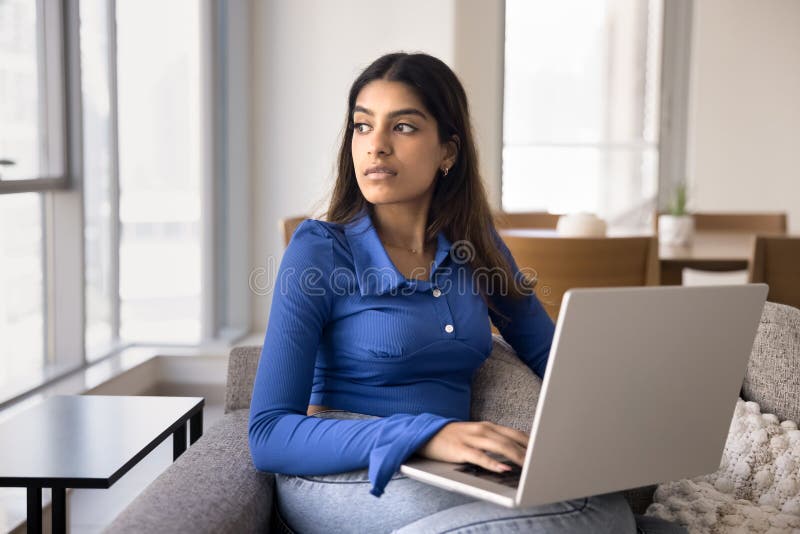 Pensive junge indische Frau, die auf einem Laptop sitzt stockfotografie