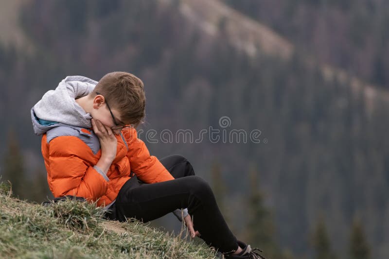 Pensive teenage guy sits on hillside and thinks about something.Hiking and travelling with children. Weekend in nature