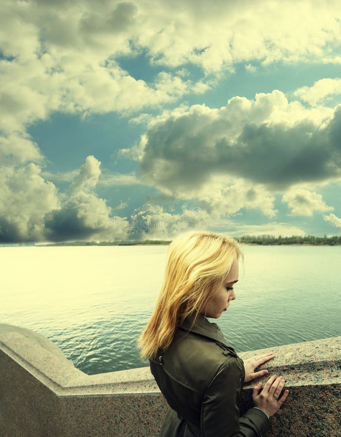 Pensive woman leaning on granite sea-wall ander sky with clouds, toned image, profile view