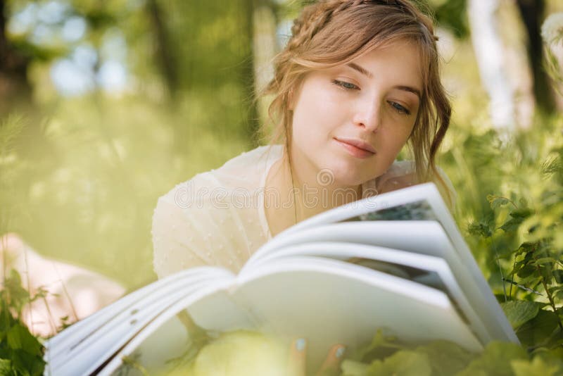 Pensive woman lying and reading magazine ourdoors