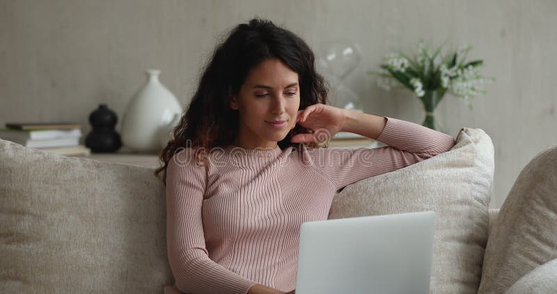 Attractive pensive woman sit on sofa working on laptop