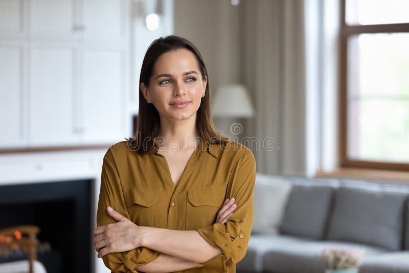 Pensive woman standing in living room smiles looks into distance