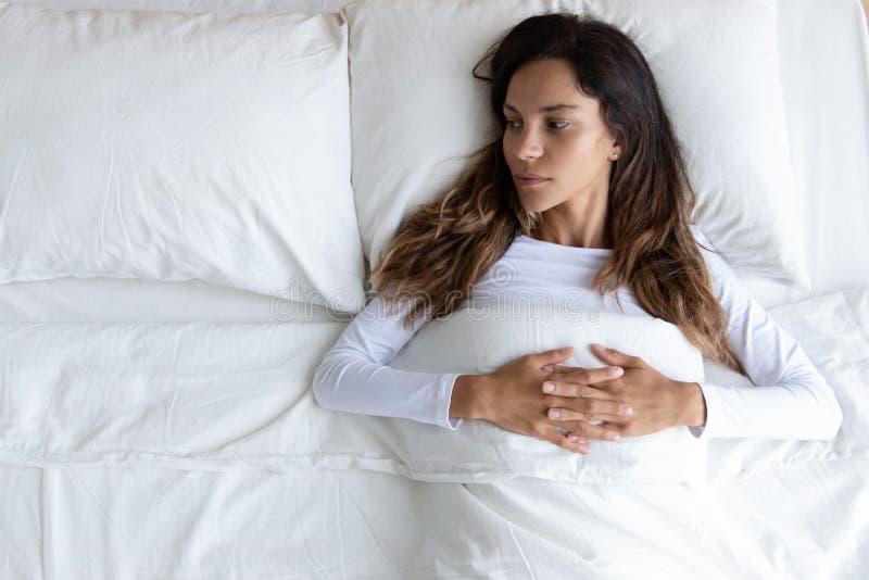 Pensive young woman lying alone in bed thinking