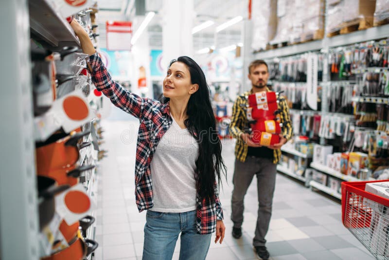 Young couple buying pans in supermarket. Male and female customers on family shopping. Man and women purchasing goods for the house. Young couple buying pans in supermarket. Male and female customers on family shopping. Man and women purchasing goods for the house