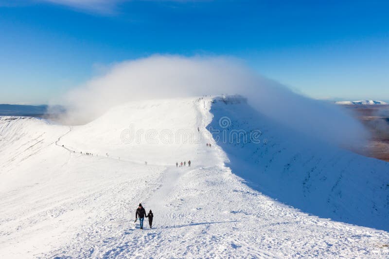 PEN-Y-FAN, WALES, UK - DECEMBER 06 2020: Large numbers of walkers and hikers enjoying fresh snow on Pen-y-Fan mountain in the Brecon Beacons National Park. This was the first snowfall of the winter season. PEN-Y-FAN, WALES, UK - DECEMBER 06 2020: Large numbers of walkers and hikers enjoying fresh snow on Pen-y-Fan mountain in the Brecon Beacons National Park. This was the first snowfall of the winter season