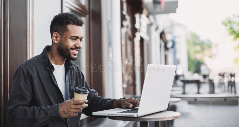 People city lifestyle young man sitting in a cafe using his laptop computer typing keyboard online outside