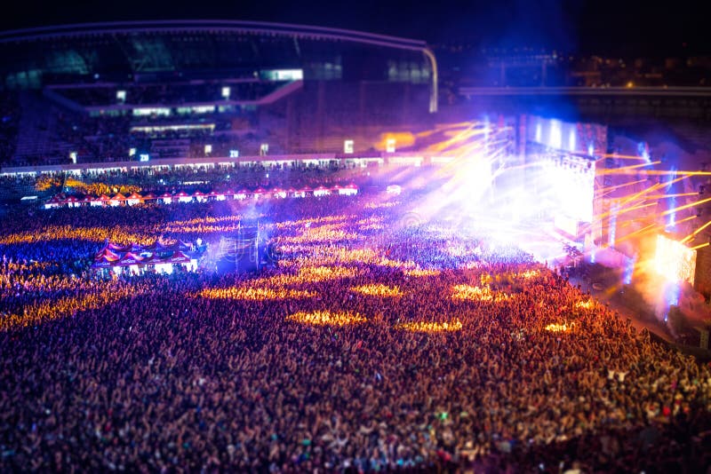 People clapping at night concert, partying and raising hands for the artist on stage. Blurry aerial view of concert crowd