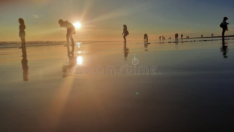 People of different cultures, ages, gender enjoying the sunset at Parangtritis Beach while standing nearly like in a row and parti