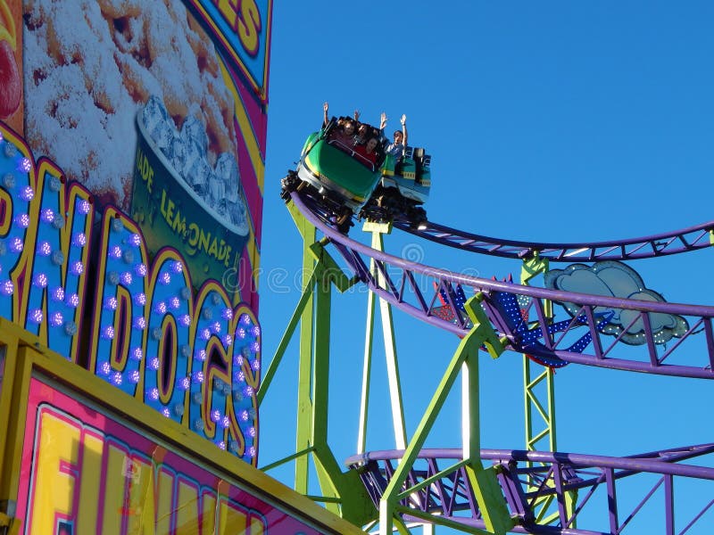 Rollercoaster dives behind flashing food stand at the fair.