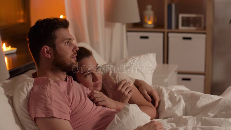 Couple watching horror on tv in bed at night