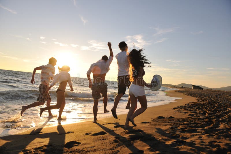 Šťastný skupina mladých lidí bavit bílé běh a skákání na beacz v době západu slunce.