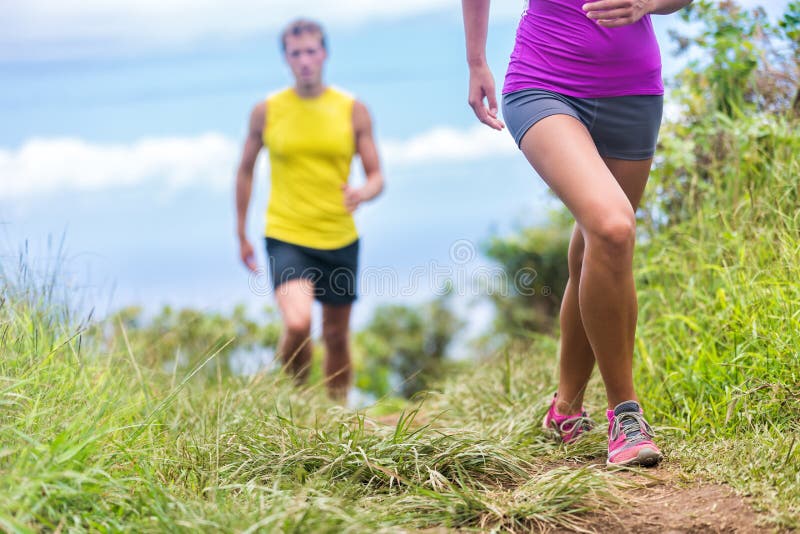 People running walking in nature on trail path. Group of runners hikers hiking in summer outdoors. Woman legs and men in the background. Fitness activity for a fit couple living a healthy lifestyle. People running walking in nature on trail path. Group of runners hikers hiking in summer outdoors. Woman legs and men in the background. Fitness activity for a fit couple living a healthy lifestyle.