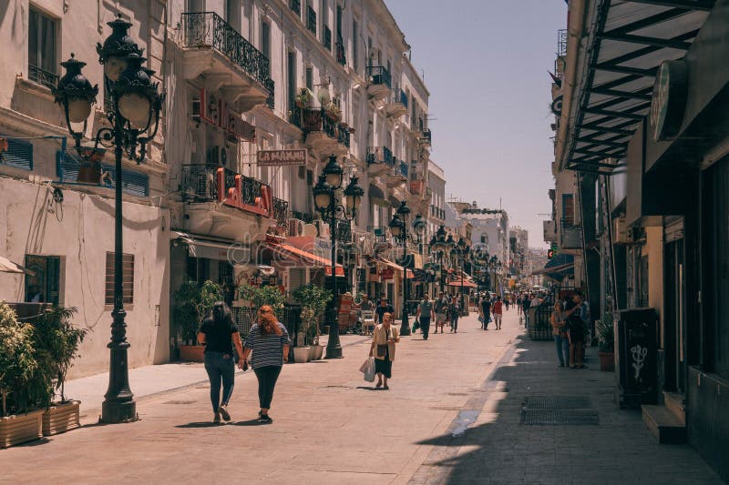 The people walk down the scenic promenade with colonial-style buildings in downtown Tunis during a hot sunny day in Tunisia