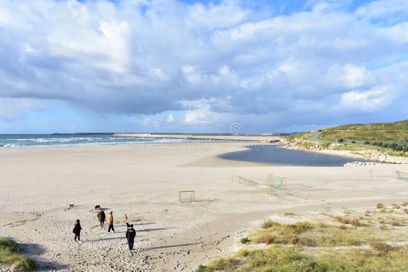 People walking with dogs on a beach with port. Cloudy day. Sabon, Spain 2 Feb 2019.