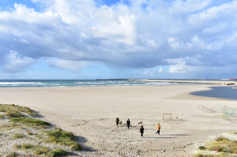 People walking with dogs on a beach with port. Cloudy day. Sabon, Spain 2 Feb 2019.