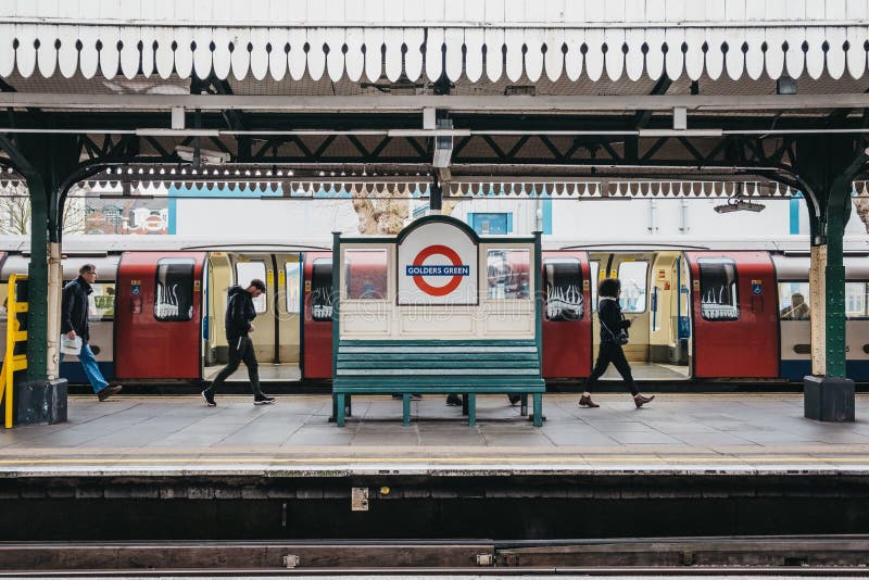 People walking past the station name sign on the outdoor platform of Golders Green tube station, London, UK