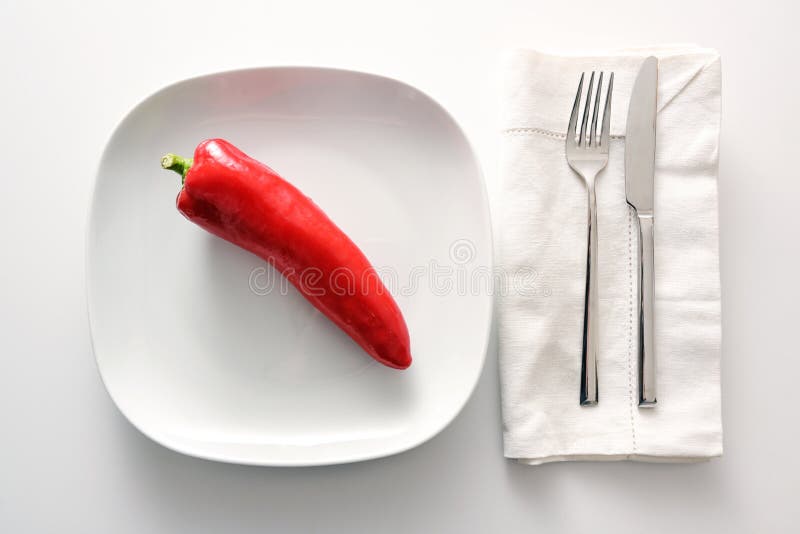 Raw red pointed sweet pepper on a white plate, cutlery and napkin beside on a bright background, healthy eating with vegetables or diet to lose weight as a good resolution in the New Year, copy space, high angle view from above. Raw red pointed sweet pepper on a white plate, cutlery and napkin beside on a bright background, healthy eating with vegetables or diet to lose weight as a good resolution in the New Year, copy space, high angle view from above