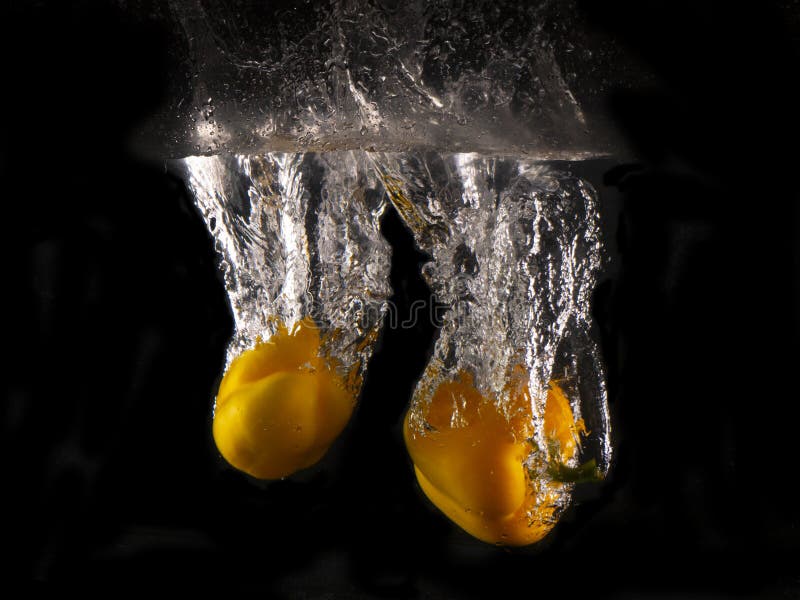 Peperone dolce giallo che cade nella spruzzatura dell'acqua sul fondo nero fotografie stock libere da diritti Peperone dolce giallo che cade nella spruzzatura dell'acqua sul fondo nero fotografie stock libere da diritti