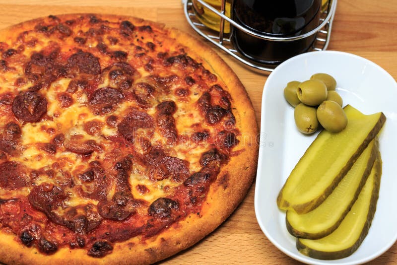 A pepperoni pizza with pickle and olives as a side stock image A pepperoni pizza with pickle and olives as a side stock image